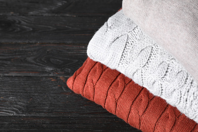 Stack of folded warm sweaters on black wooden table, closeup