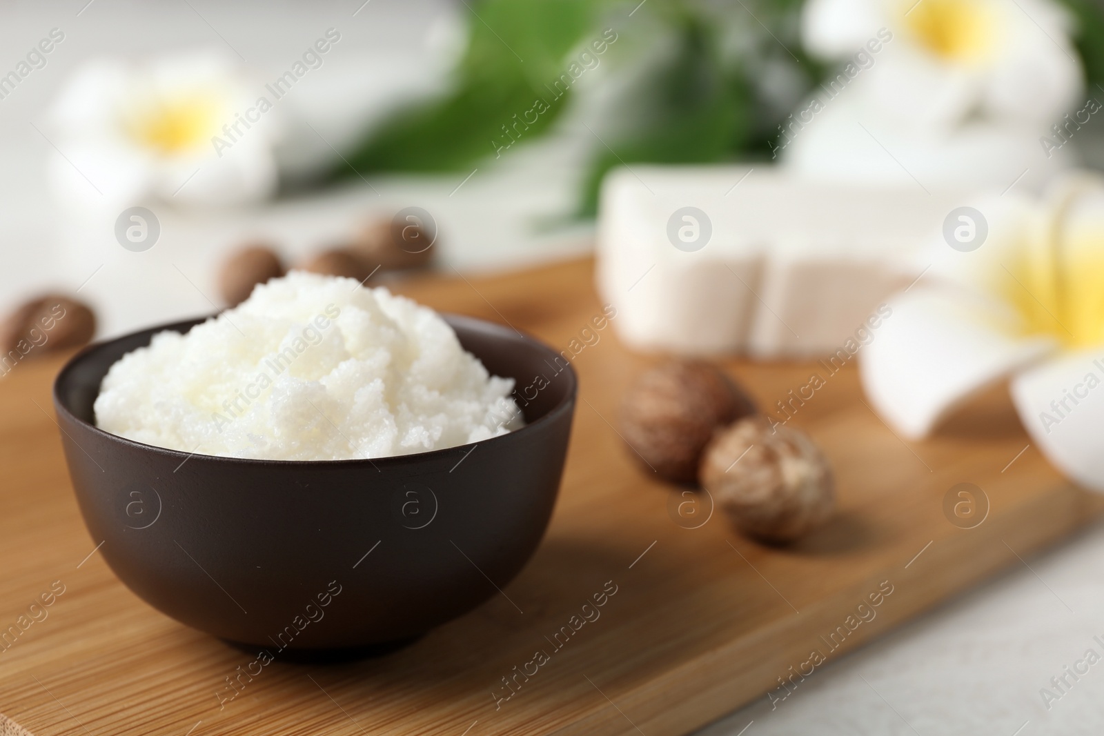 Photo of Shea butter in bowl and nuts on wooden board, closeup. Space for text