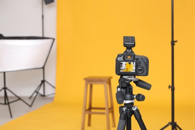 Photo of Camera on tripod, bar stool and professional lighting equipment in modern photo studio, space for text