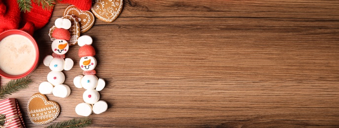 Flat lay composition with funny snowmen made of marshmallows on wooden table, space for text