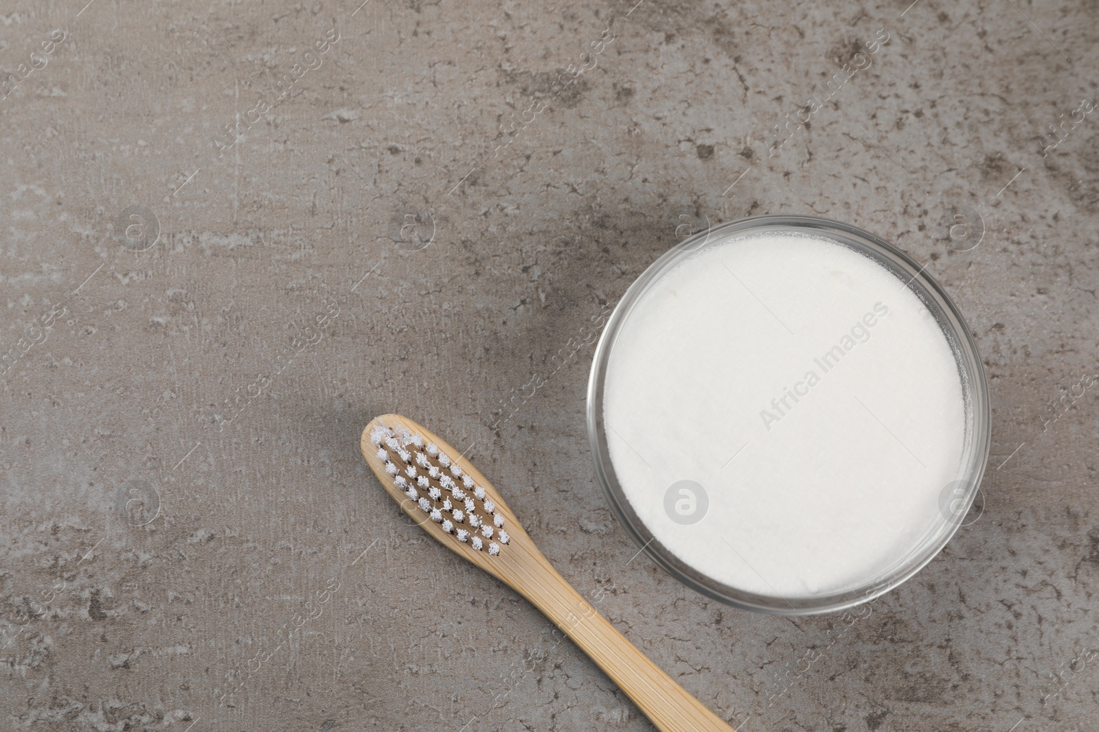 Photo of Bamboo toothbrush and bowl of baking soda on grey table, flat lay. Space for text