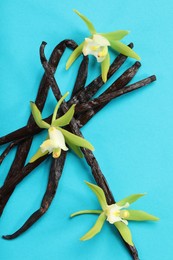 Photo of Vanilla pods and beautiful flowers on light blue background, top view