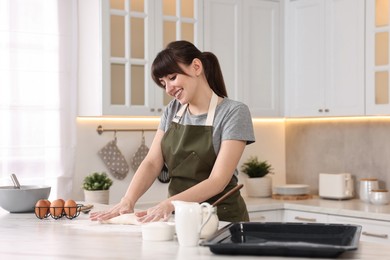 Photo of Happy young housewife kneading dough at white marble table in kitchen