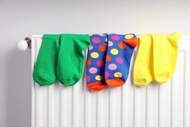 Different colorful socks on heating radiator near white wall