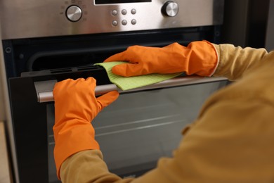 Photo of Woman with microfiber cloth cleaning electric oven in kitchen, closeup