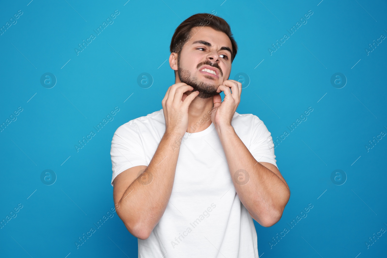 Photo of Young man scratching face on color background. Annoying itch