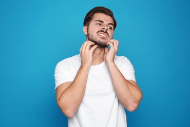 Young man scratching face on color background. Annoying itch