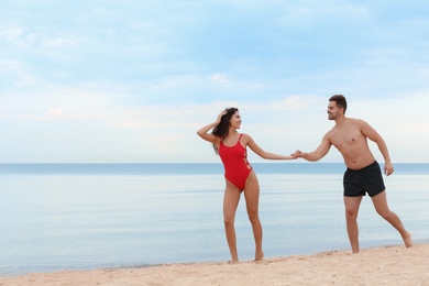 Happy young couple walking together on beach near sea