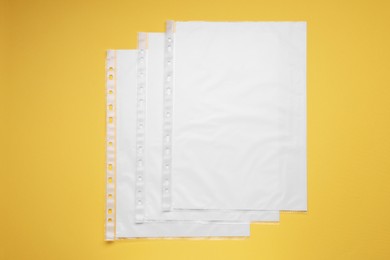 Punched pockets with paper sheets on yellow background, flat lay. Space for text