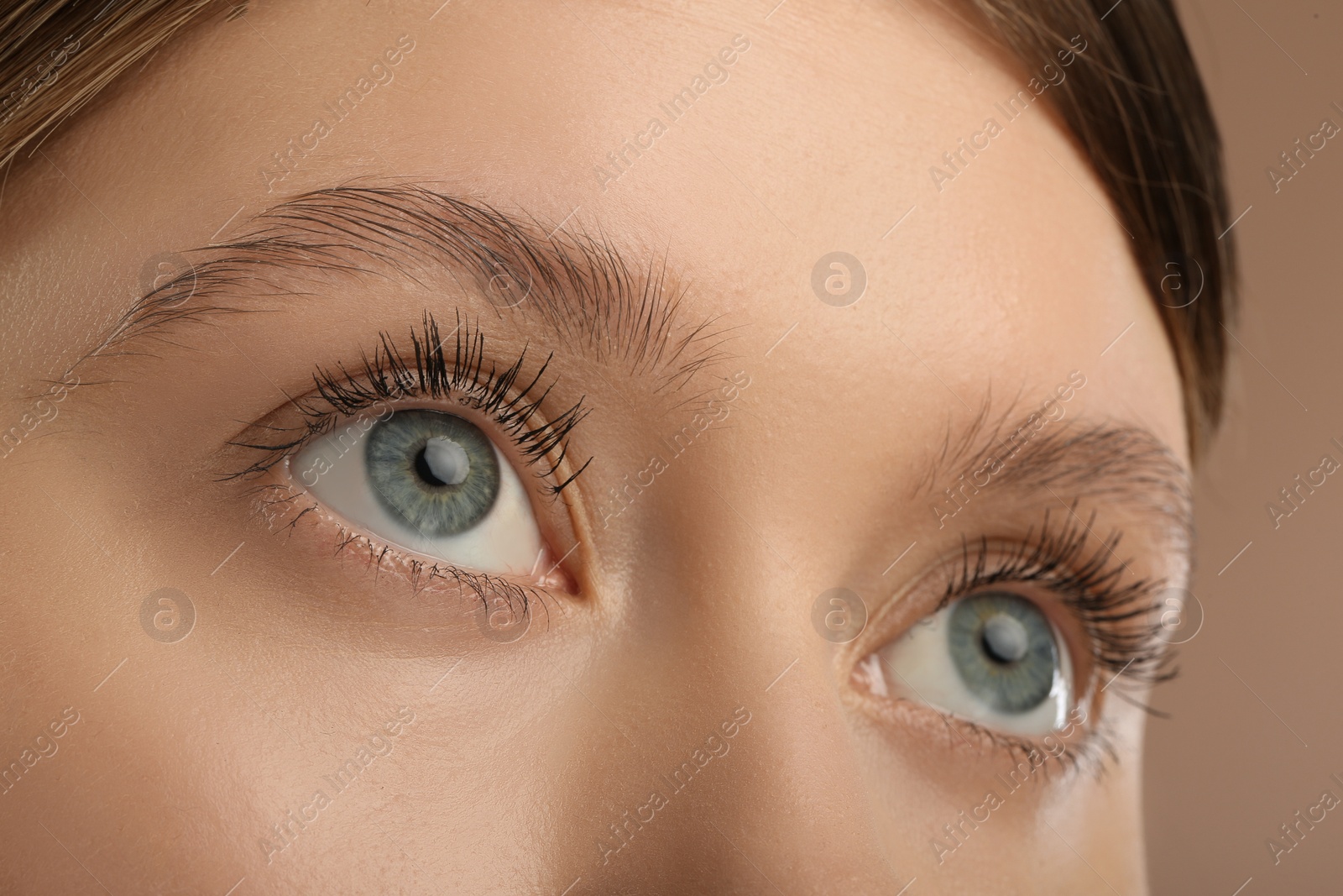 Photo of Woman with long eyelashes after mascara applying against light brown background, closeup