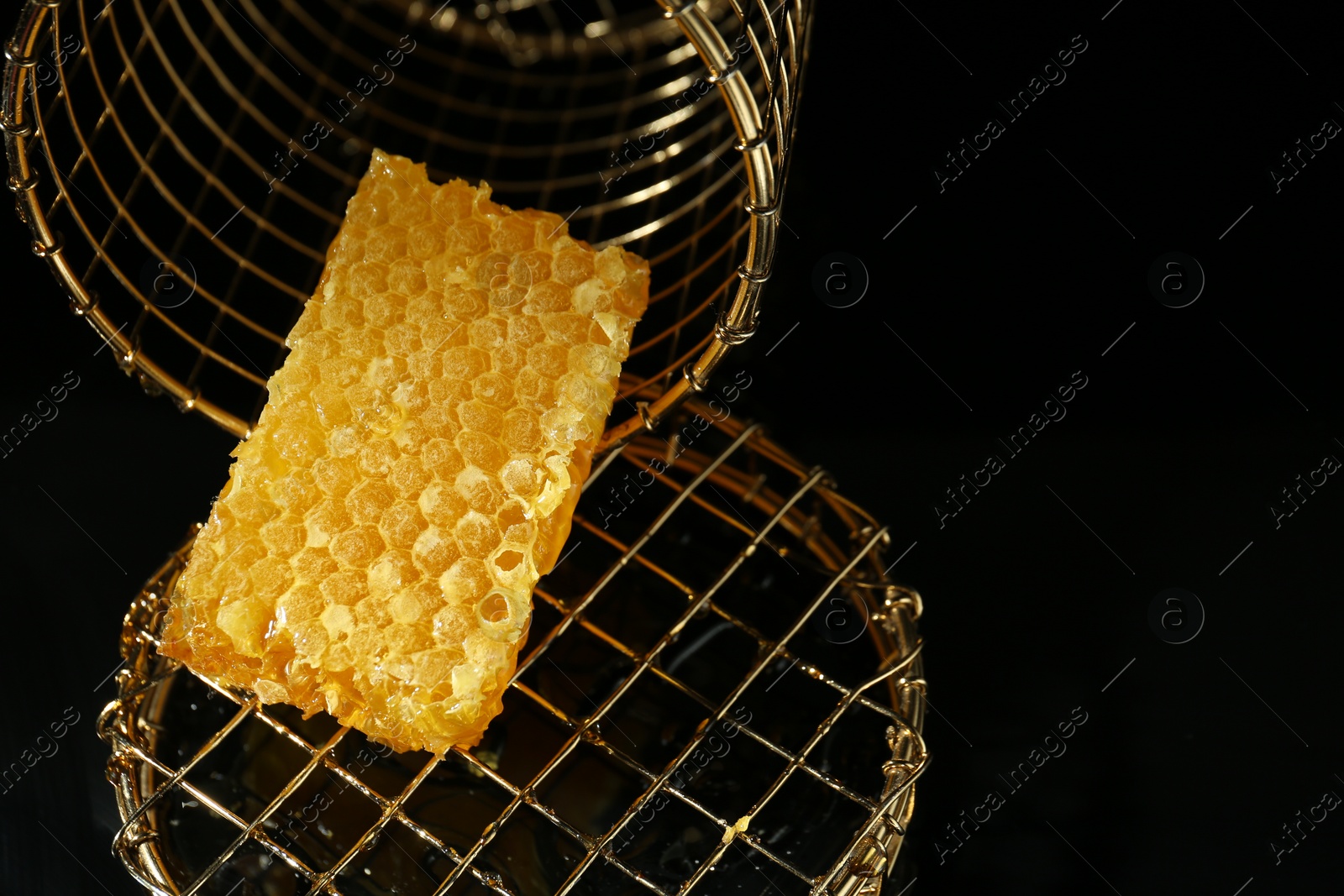Photo of Piece of natural honeycomb with tasty honey on black background, space for text