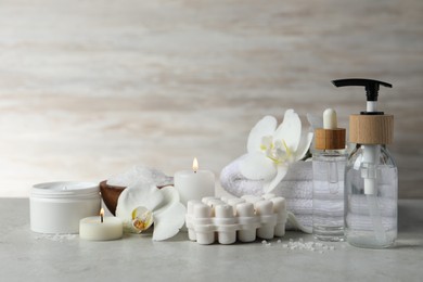 Photo of Beautiful composition with different spa products, burning candles and flowers on light grey table. Space for text