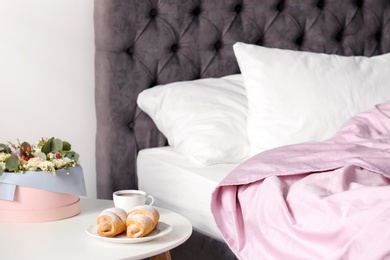 Plate with delicious croissants and cup of coffee on table near bed