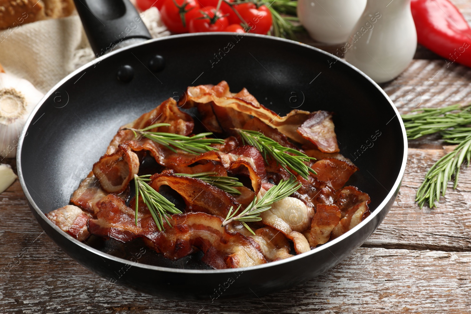 Photo of Delicious bacon slices in frying pan and products on wooden table, closeup