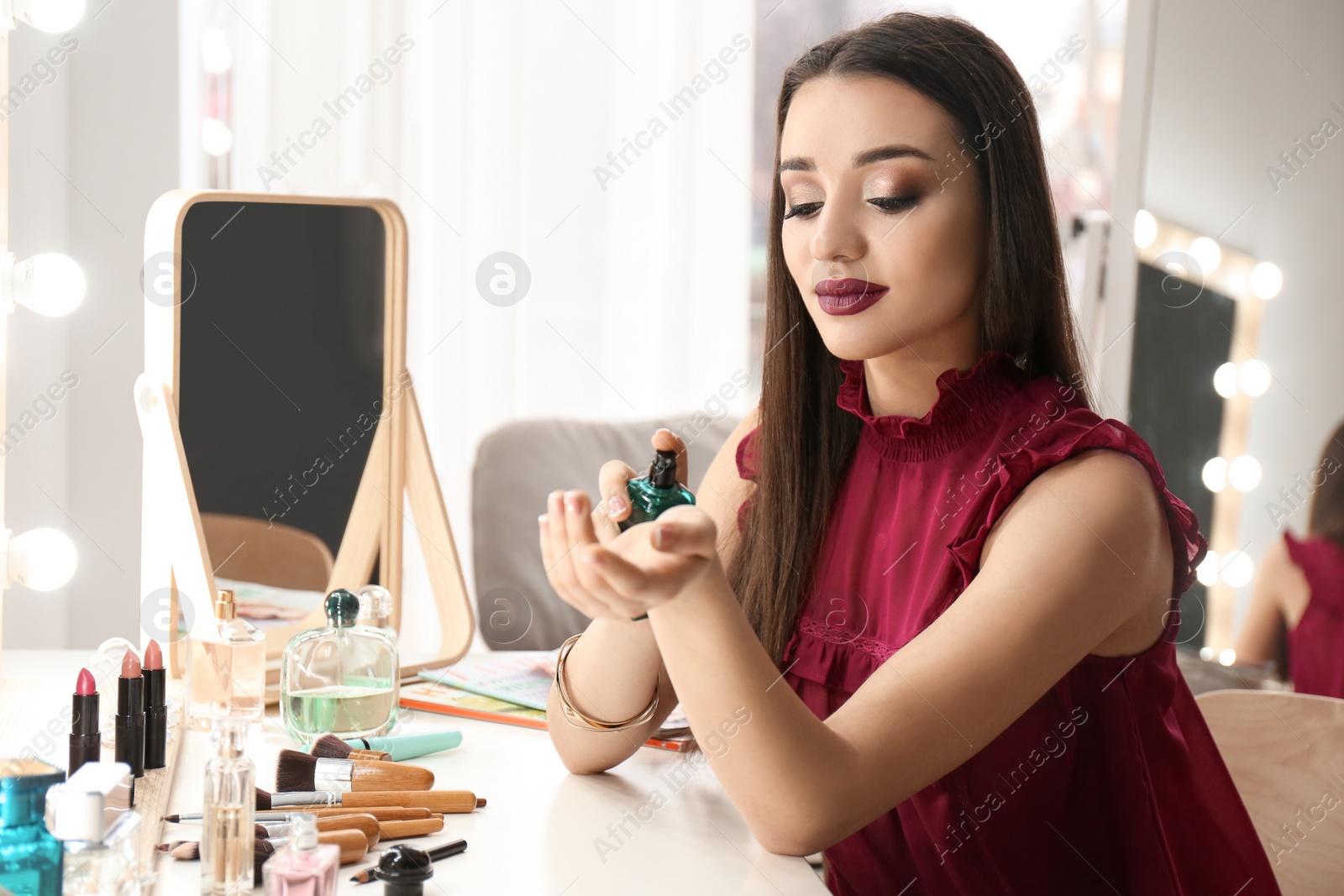 Photo of Portrait of beautiful woman with bright makeup applying perfume indoors