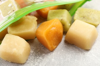 Photo of Different frozen fruit puree cubes in plastic bag on table, closeup