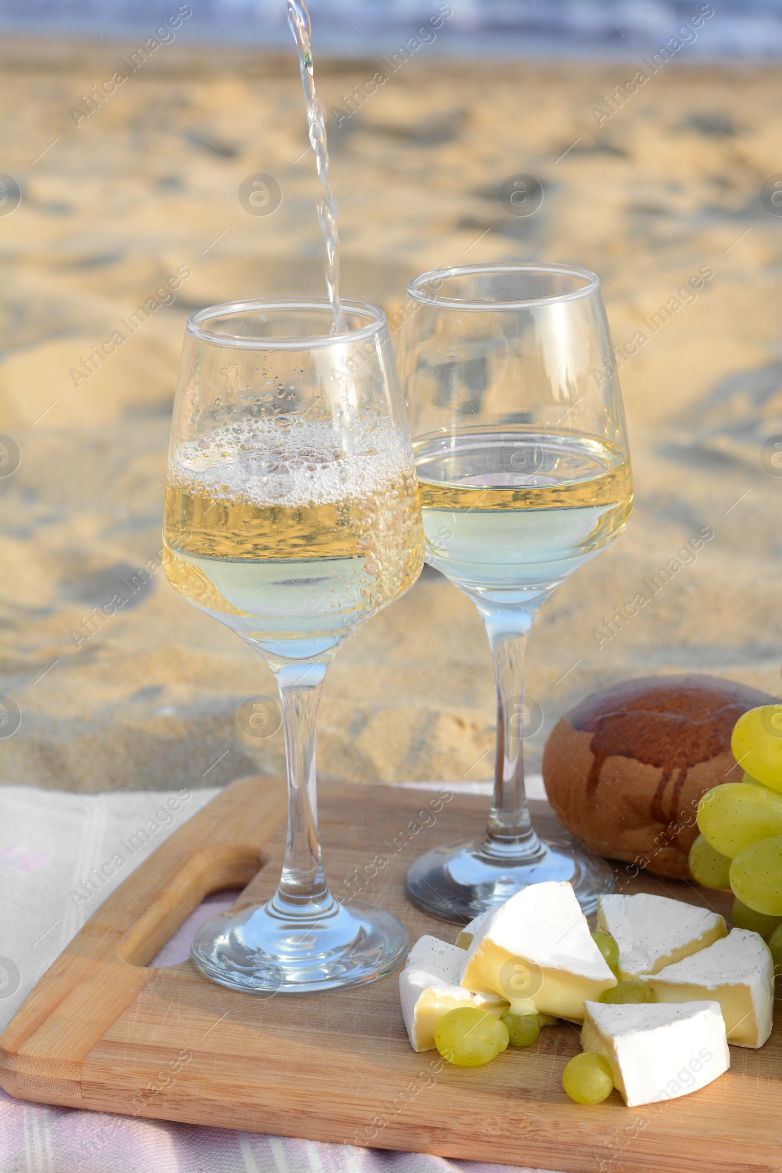 Photo of Pouring white wine into glasses on picnic blanket near sea