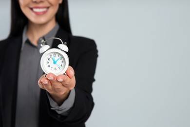 Photo of Businesswoman holding alarm clock on light grey background, closeup with space for text. Time management