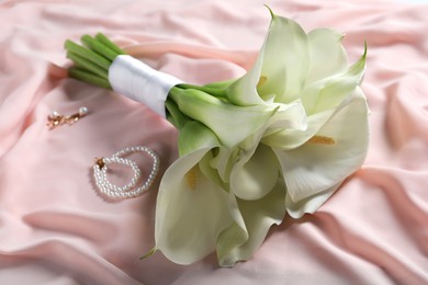 Beautiful calla lily flowers tied with ribbon, bottle of perfume and jewelry on pink fabric