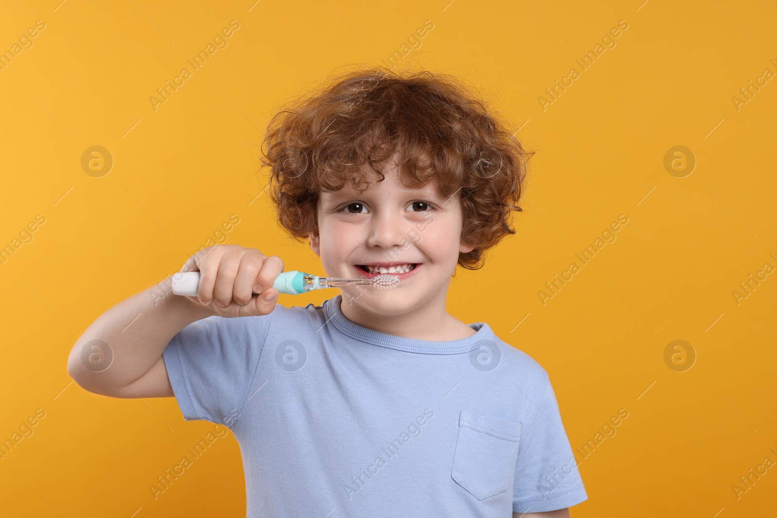 Photo of Cute little boy holding electric toothbrush on yellow background