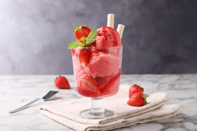 Photo of Tasty strawberry ice cream with fresh berries and wafer rolls in glass dessert bowl on white marble table
