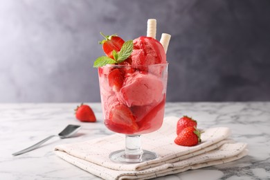 Tasty strawberry ice cream with fresh berries and wafer rolls in glass dessert bowl on white marble table