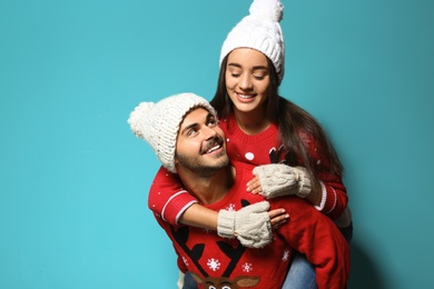 Photo of Young couple in Christmas sweaters and knitted hats on color background