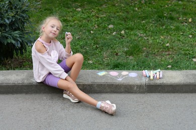Photo of Little child drawing balloons and ukrainian flag with chalk on curb outdoors, space for text