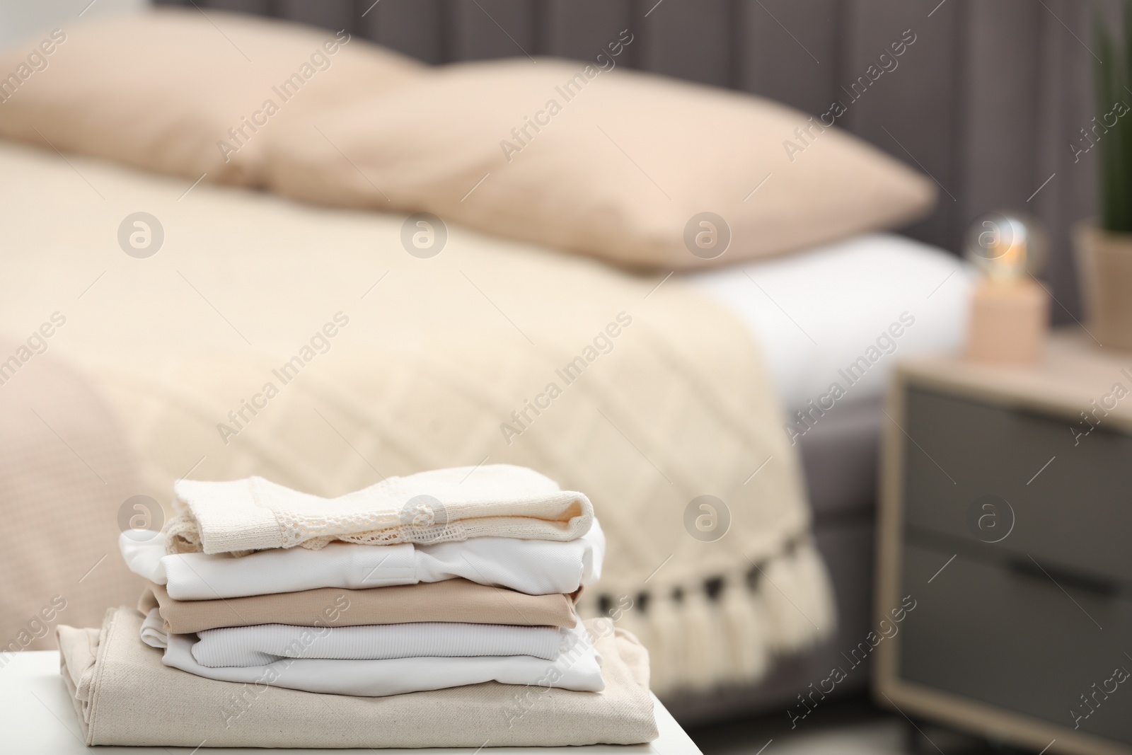 Photo of Stack of different folded clothes on bedside bench indoors, closeup. Space for text