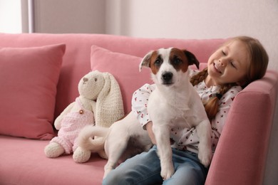 Photo of Cute little girl with her dog on sofa, space for text. Childhood pet