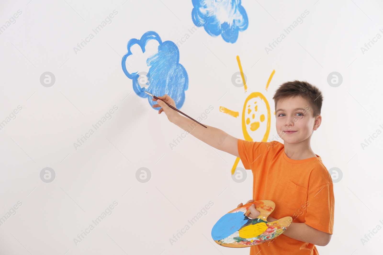 Photo of Little child painting cloud on white wall in room