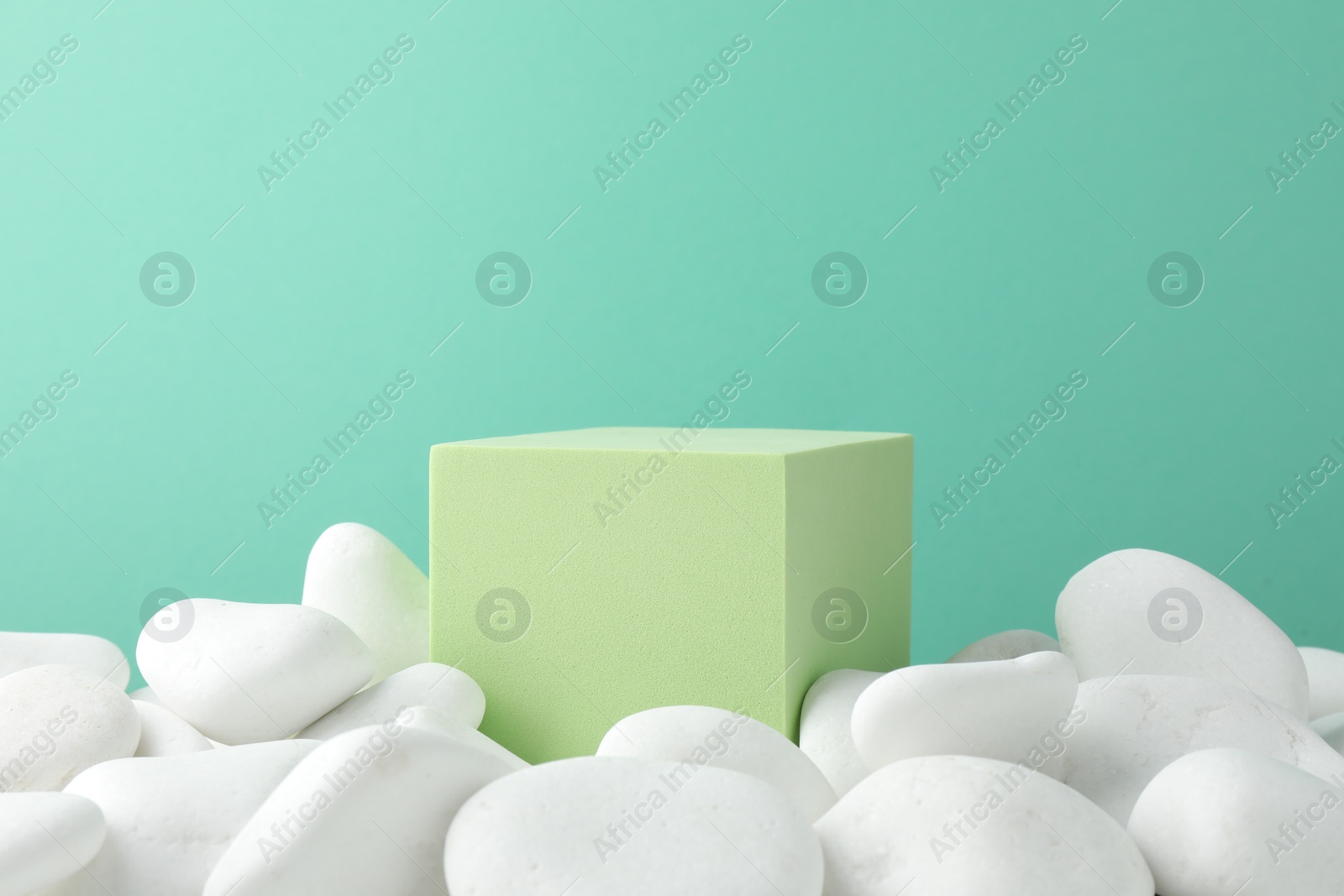 Photo of Presentation for product. Light green cube podium and white pebbles on color background. Space for text