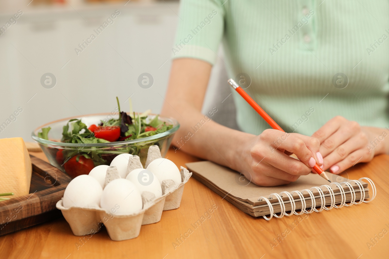 Photo of Woman writing in notebook near products at table, closeup. Keto diet