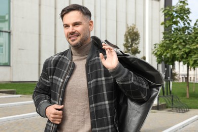 Man holding garment cover with clothes outdoors. Dry-cleaning service