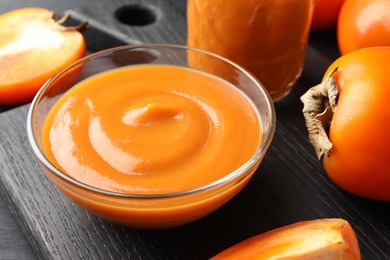 Photo of Delicious persimmon jam in glass bowl and fresh fruits on dark gray wooden table, closeup