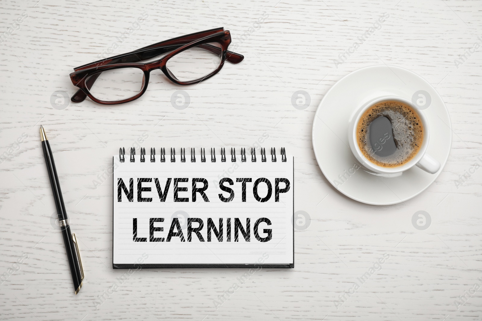 Image of Notebook with phrase NEVER STOP LEARNING,  cup of coffee and glasses on white wooden background, flat lay