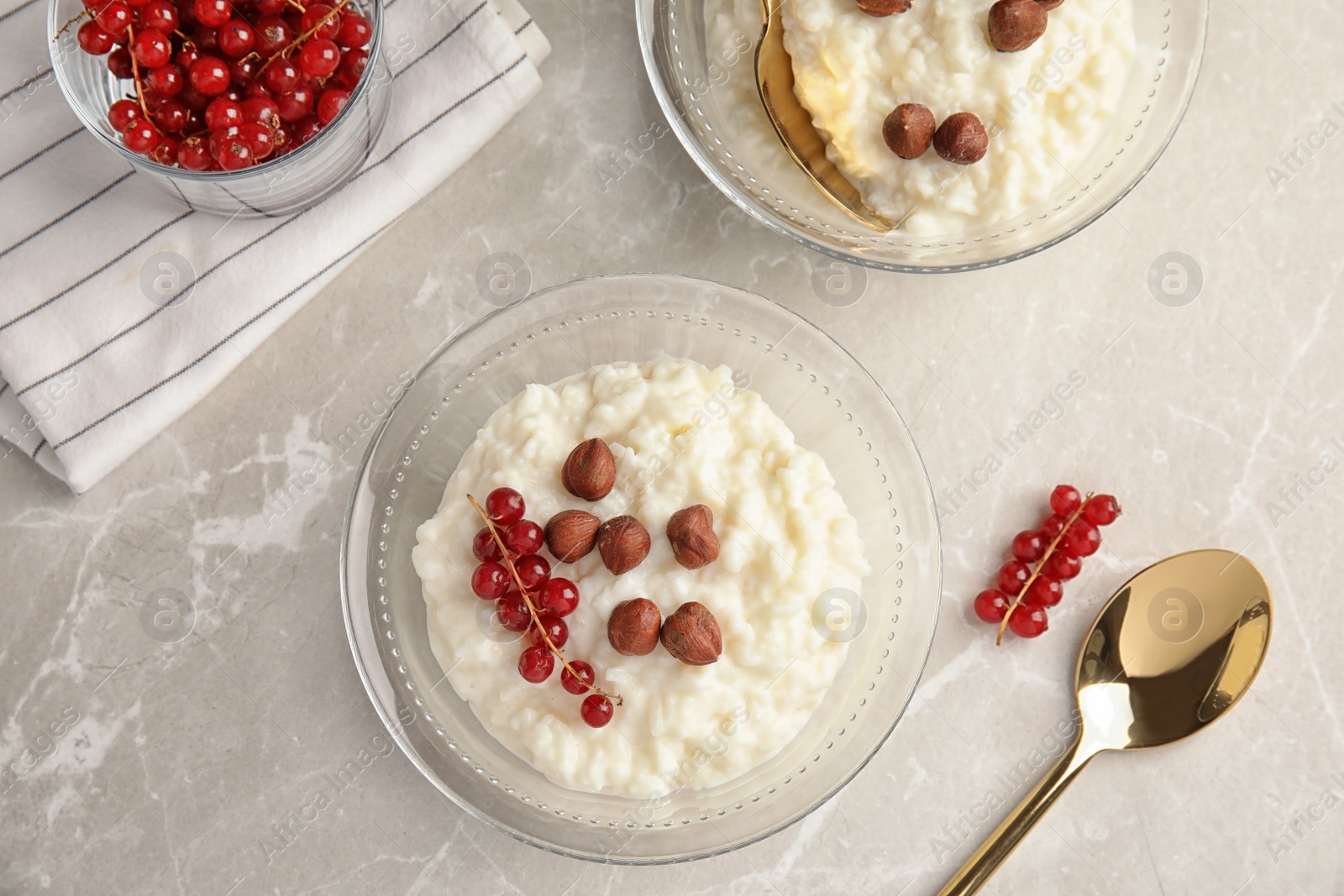 Photo of Creamy rice pudding with red currant and hazelnuts in bowls served on grey table, top view