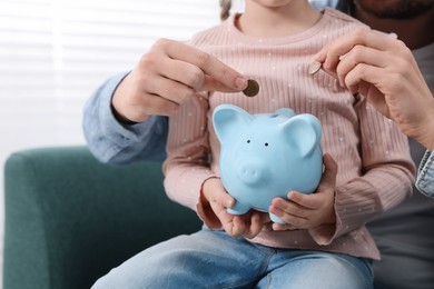 Photo of Family budget. Little girl and her parents putting coins into piggy bank at home, closeup