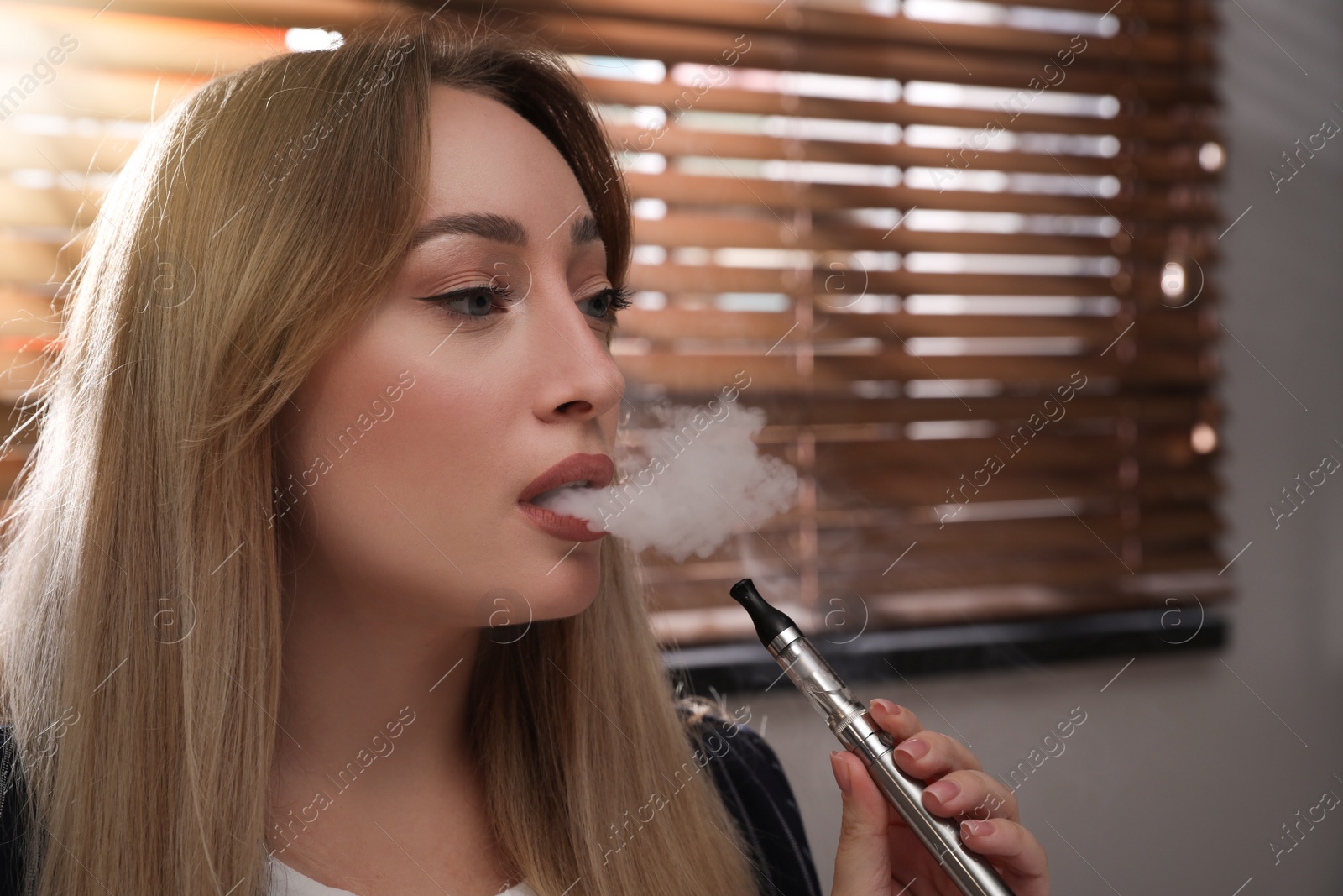 Photo of Beautiful young woman using electronic cigarette indoors