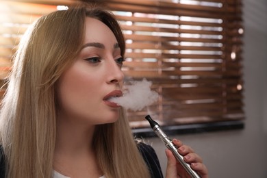Beautiful young woman using electronic cigarette indoors