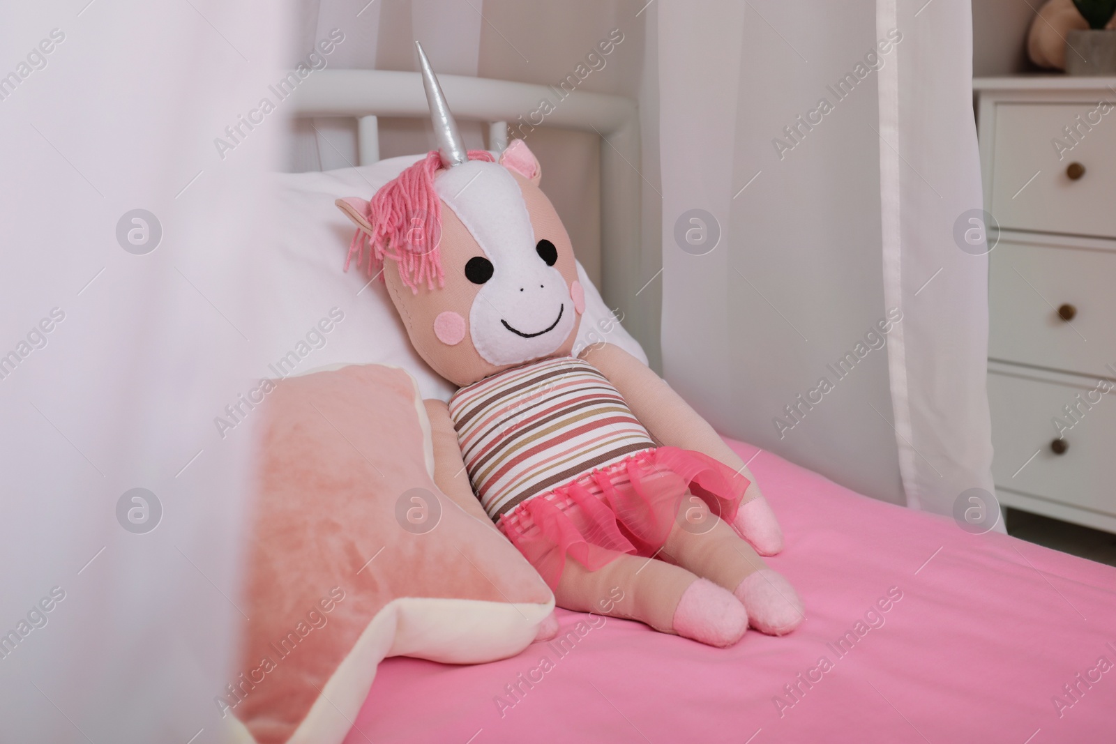 Photo of Soft toy unicorn and star shaped cushion on bed in child's room. Interior design