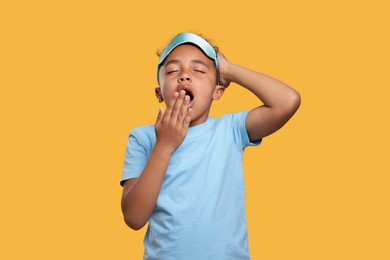 Photo of Boy with sleep mask yawning on yellow background. Insomnia problem