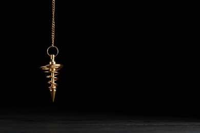 Stylish pendulum above table on black background, space for text. Hypnotherapy session