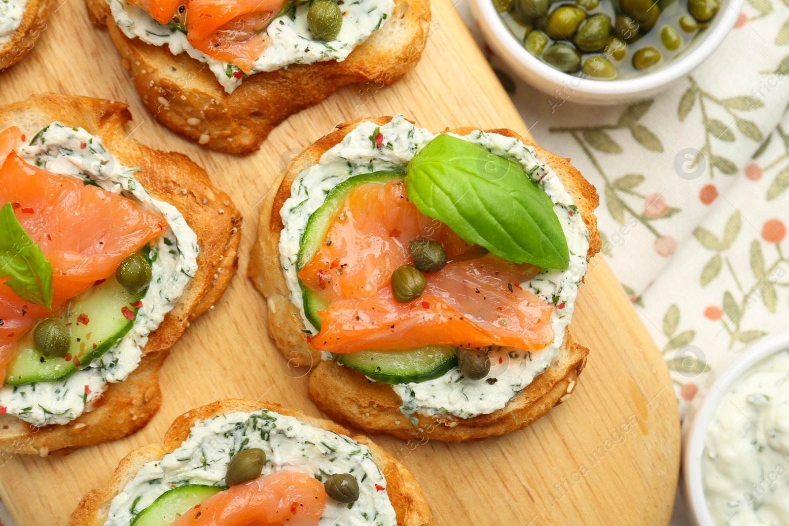 Photo of Tasty canapes with salmon, capers, cucumber and sauce on table, top view