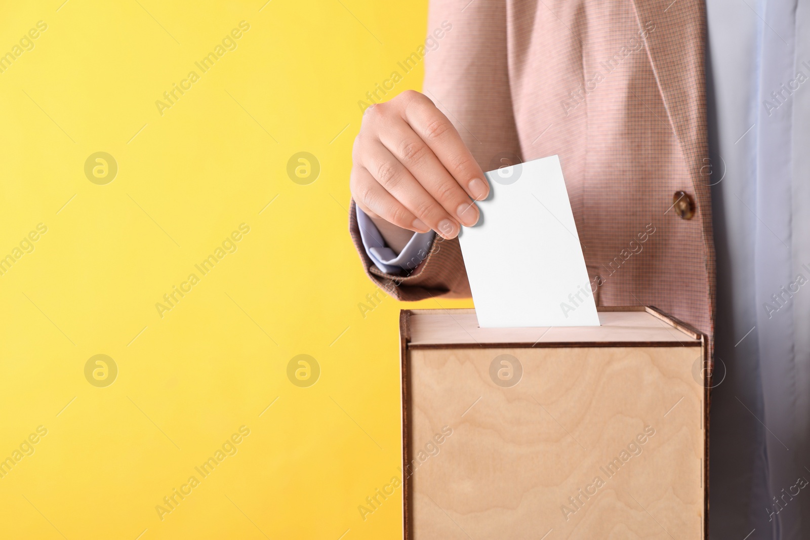 Photo of Woman putting her vote into ballot box on orange background, closeup. Space for text