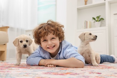 Photo of Little boy lying with cute puppies on carpet at home