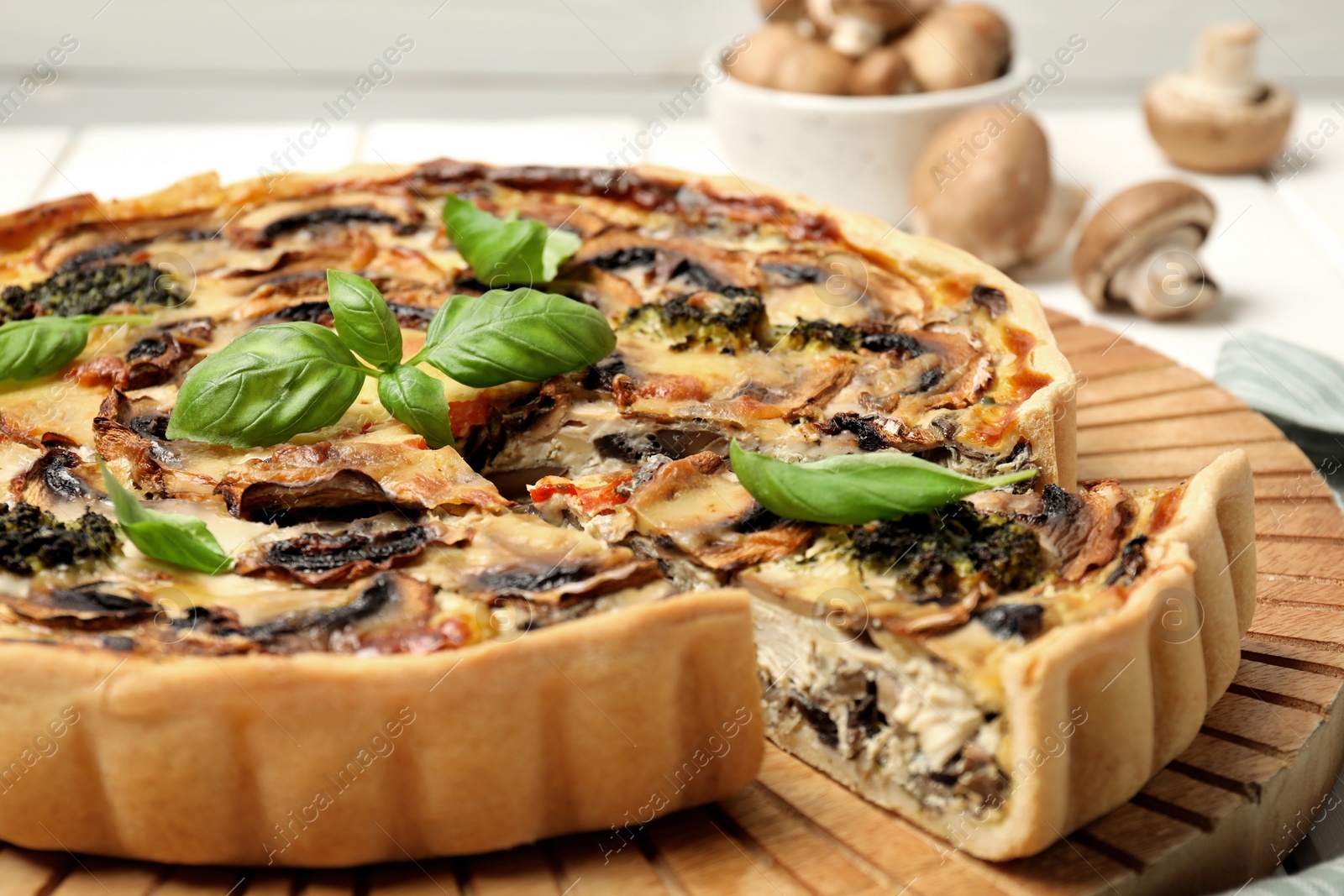 Photo of Delicious quiche with mushrooms and basil on wooden board, closeup