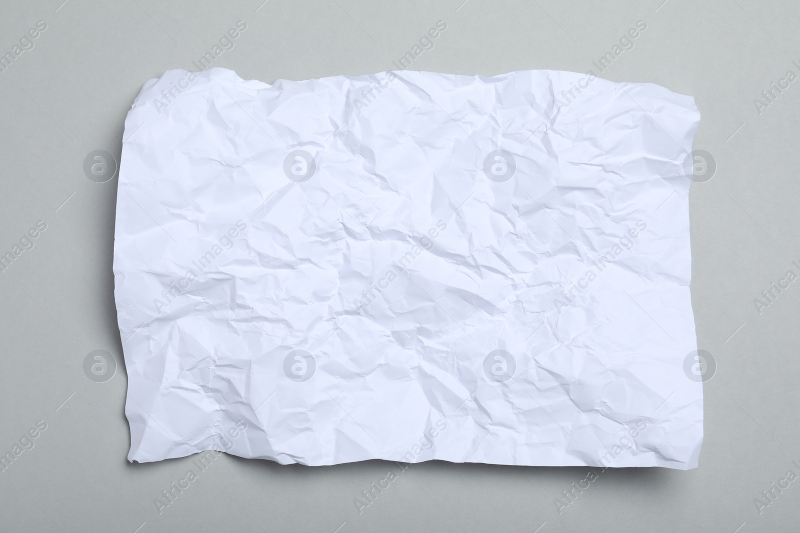 Photo of Sheet of white crumpled paper on grey background, top view