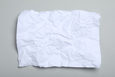 Sheet of white crumpled paper on grey background, top view