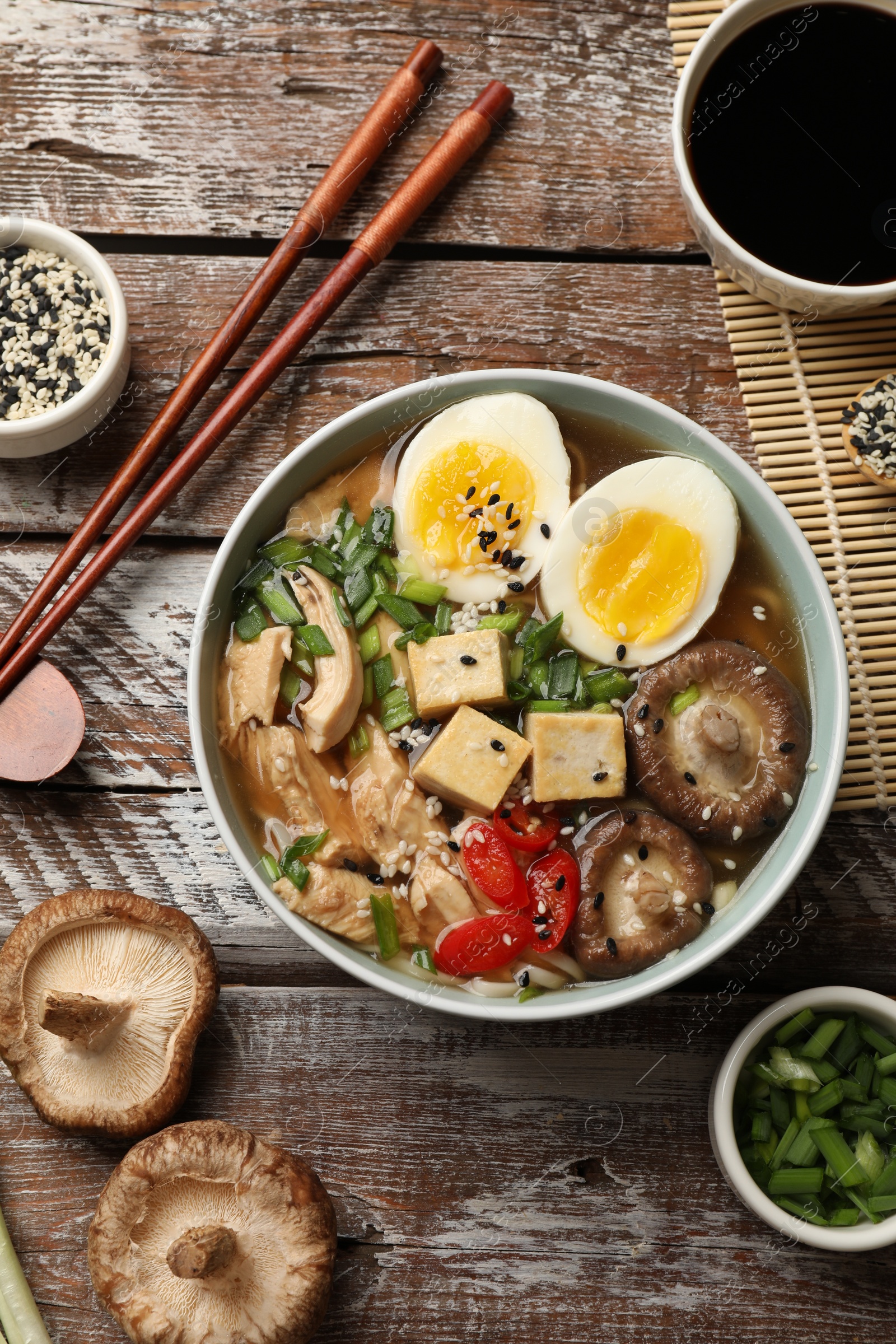 Photo of Noodle soup. Bowl of delicious ramen, ingredients and chopsticks on wooden table, flat lay